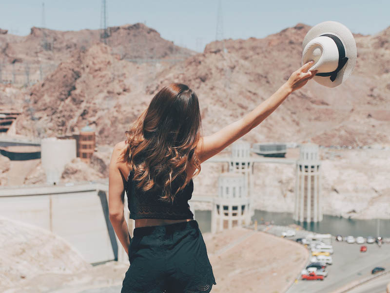 A woman with her back turned to the camera, posing in front of the Hoover Dam