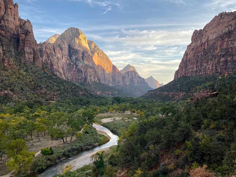 A river winding through a green valley, durrounded by rocky mountains at Zion National Park