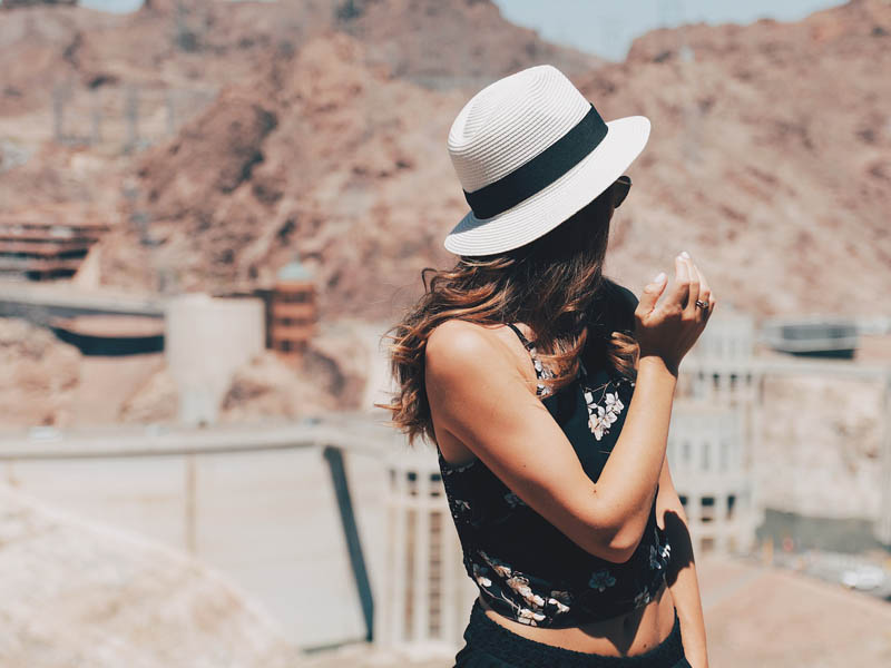 A woman with her head turned away from the camera, in front of the Hoover Dam