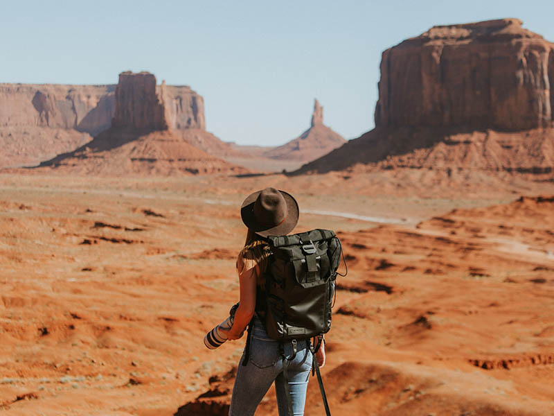 A woman with her back turned, holding a camera, at Monument Valley